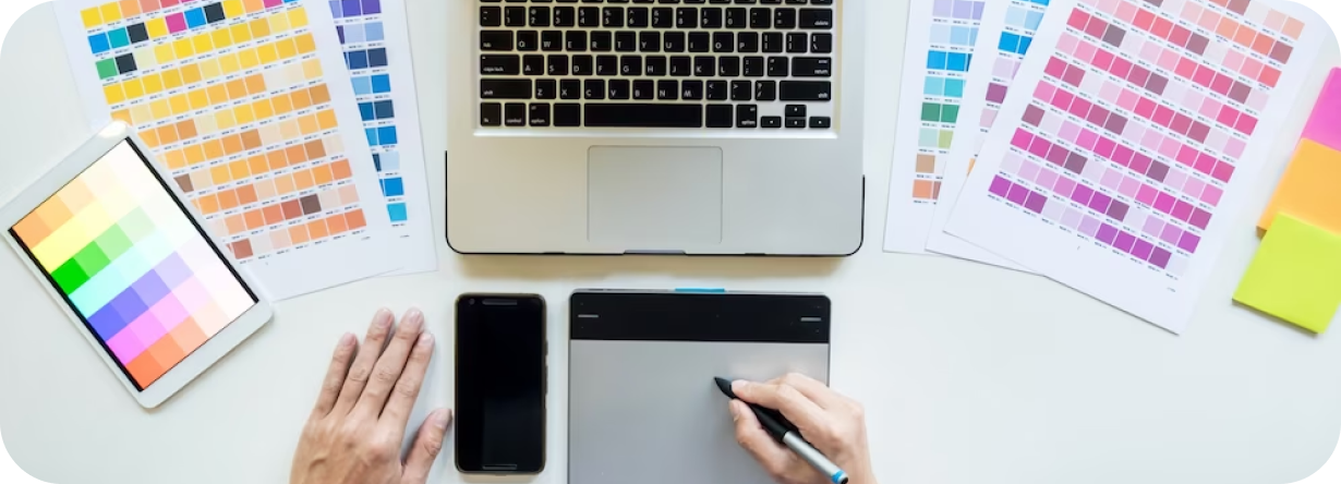 Se muestra una computadora apoyada en una mesa y a su alrededor se muestran paletas de colores y dispositivos de diseño