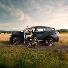 kiaaaaaa foto de carro kia, con persona con movilidad reducida pasandose de una silla de rueda al interior del carro, en un campo abierto